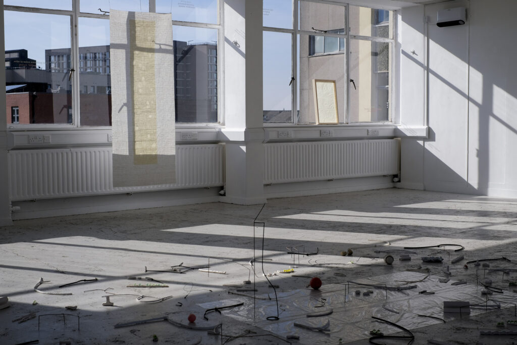 Two fragile paper works hung before well-lit windows with light streaming through casting shadows
