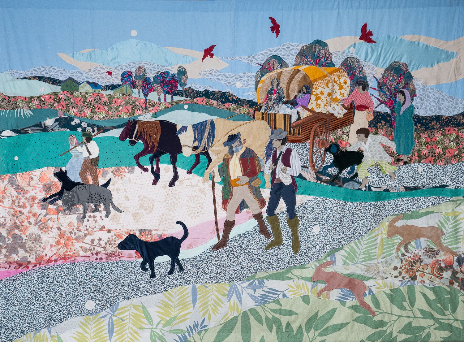a colourful textile work depicting a group of people and animals moving trough a landscape with a horse-drawn caravan