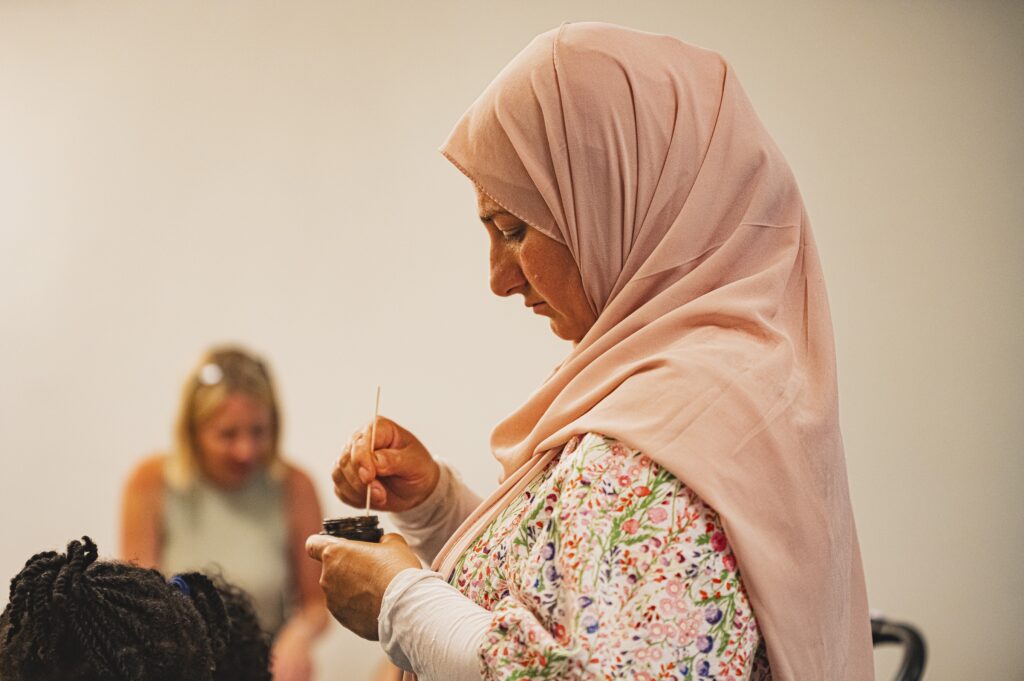 A photo of a woman with a pink headscarf looks down at a small pot that she is stirring.