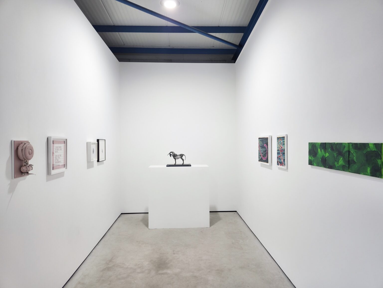 a gallery space with small framed works and a sculpture of a horse