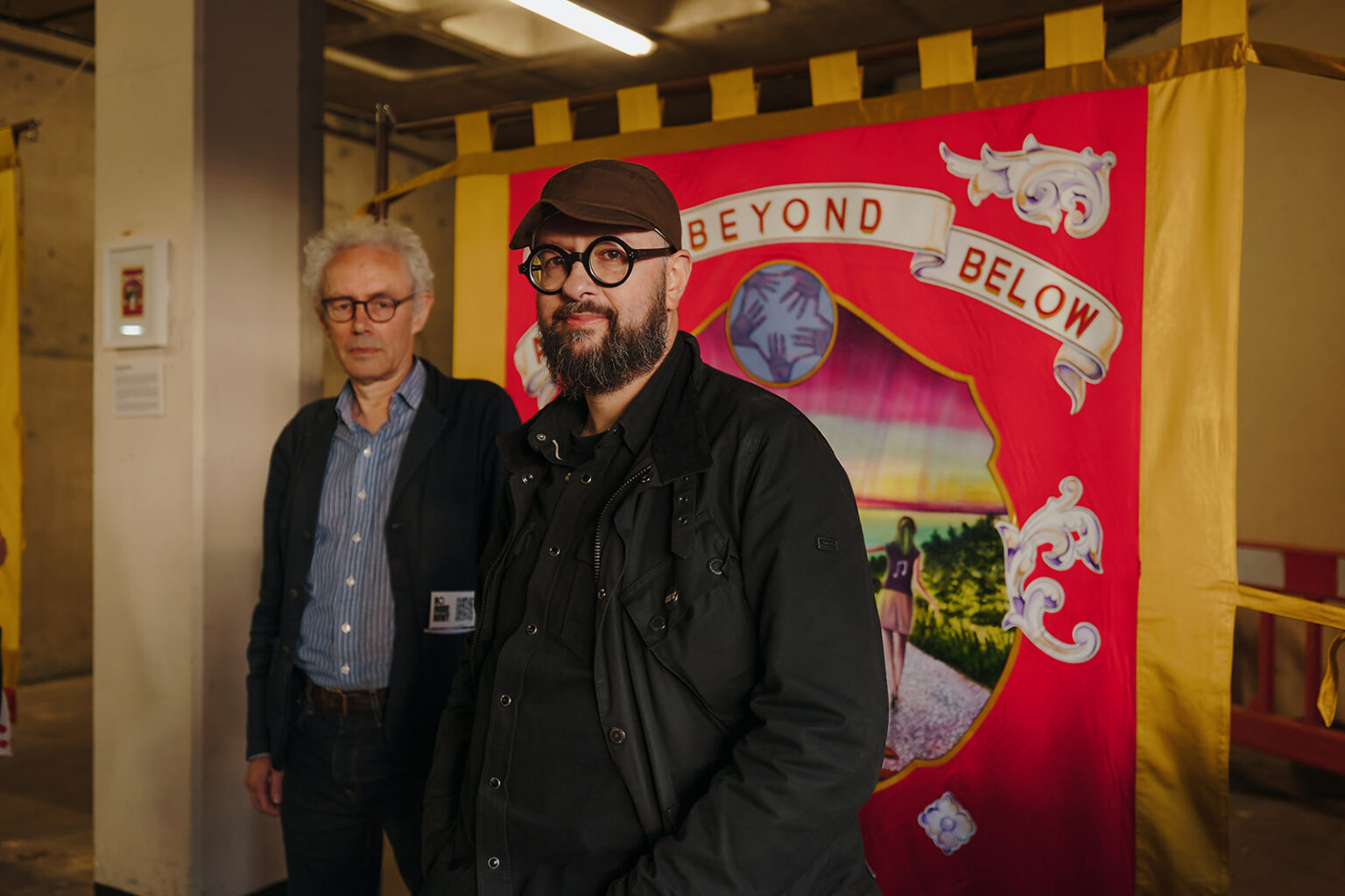 Two men stand in front of a red banner