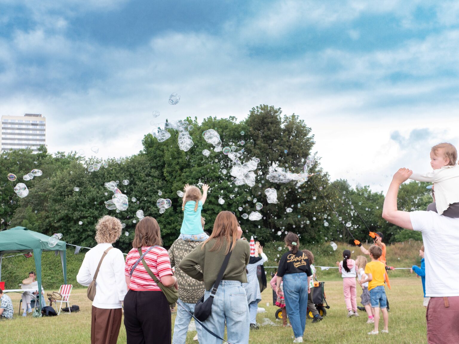 A group of adults and children reaching towards bubbles in the sky.